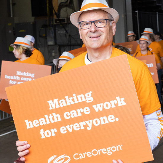 careoregon-mission 1 Group of people in orange attire holding signs that read ‘Making health care work for everyone. CareOregon,’ in a parade.