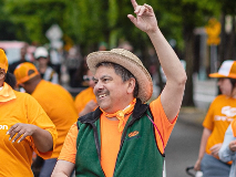 CareOregon Employee in a Green vest and orange t shirt waving his hand at a parade.