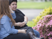 Dos personas sentadas en un banco frente a unas flores, hablando.