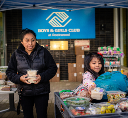 FamilyMarket_2022_JasonQuigley Person and child in front of a table full of food items at the CareOregon Boys & Girls Club at Rockwood.