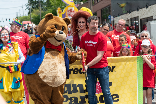 Red t-shirt-clad participants in a festive parade, holding a yellow banner, a person in a bear costume and a clown