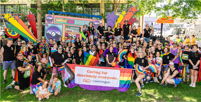 A group of people at a pride event, holding a banner that says ‘Caring for absolutely everyone’ with a CareOregon logo