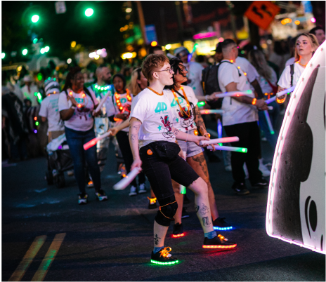 Starlight Parade_2023_JasonQuigley-3 A group of people wearing colorful attire and light-up shoes, participating in a nighttime parade.