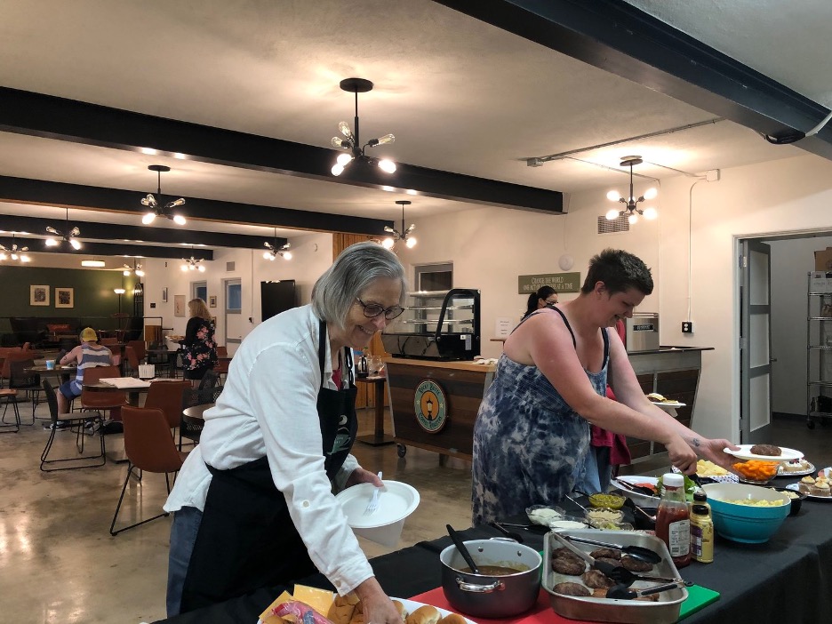 Dos mujeres sirviéndose comida de una mesa de cooperación.