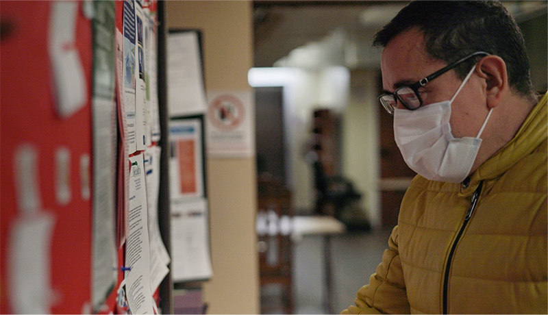 A man wearing a mask looks at a bulletin board with lots of flyers.