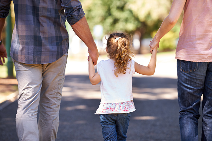 A girl is seen from behind holding the hands of two adults