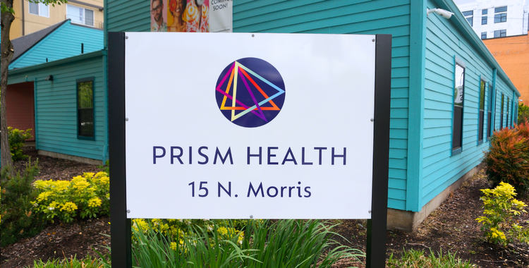 Un cartel que dice Prism Health, con una edificación azul detrás.