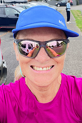 Close up of a woman's face, smiling, wearing sunglasses, in a blue cap and fuscia shirt