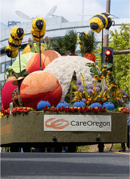 Colorful parade float with oversized bees and flowers, sponsored by CareOregon. 
