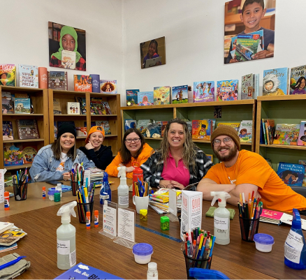 A group of people sitting at a table in an elementary school classroom, with bookshelves behind them