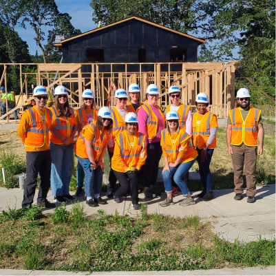 A group of people wearing safety vests and white helmets on a housing construction site