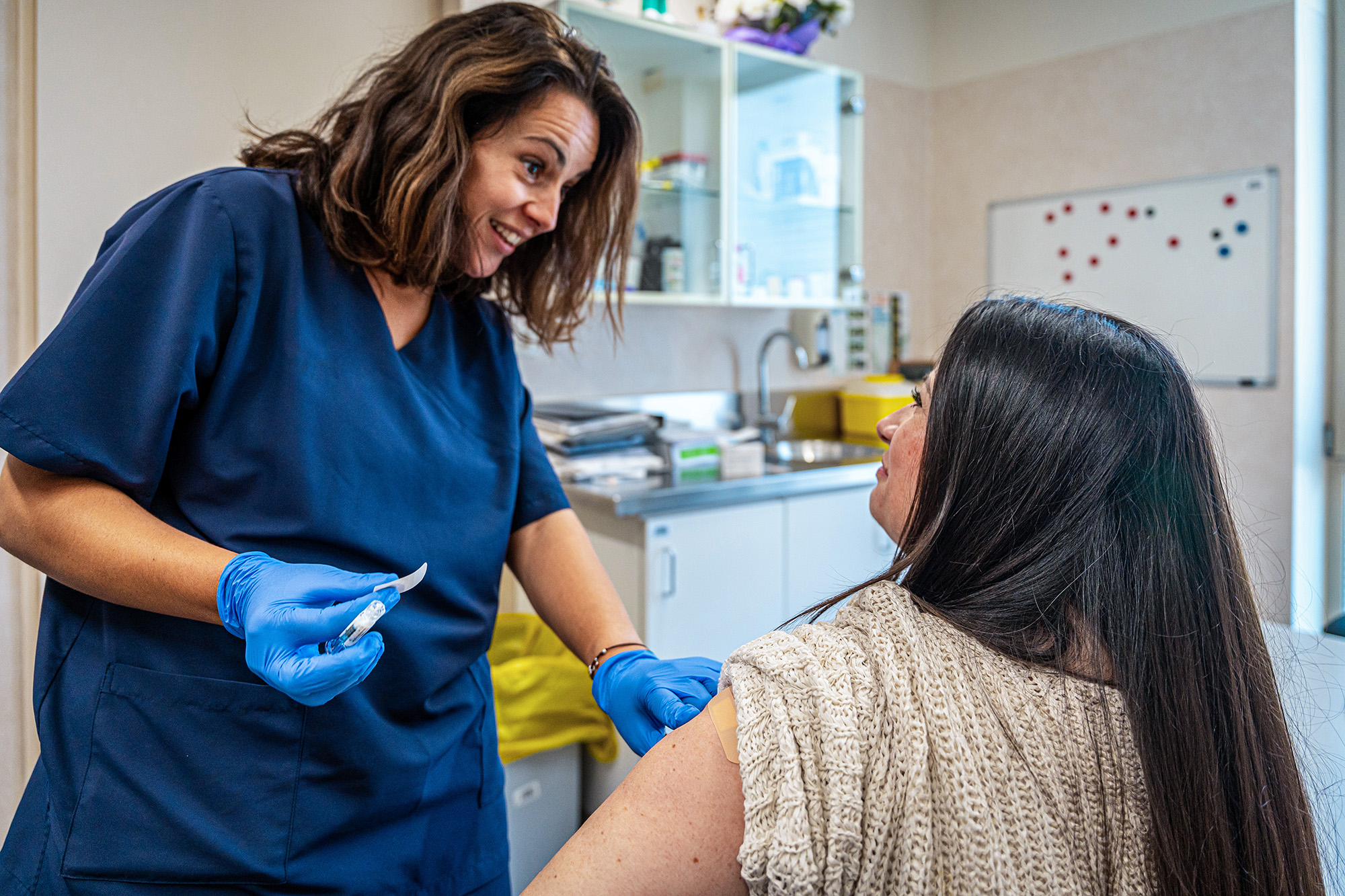 A woman about to recieve a flu shot from a provider in gloves and scrubs.