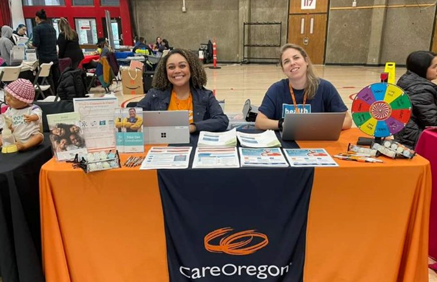 Two people sit at a table that reads CareOregon with brochures and flyers